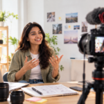 Filmmaker explaining a short film making course lesson to a camera, with a storyboard notebook and lenses on the desk